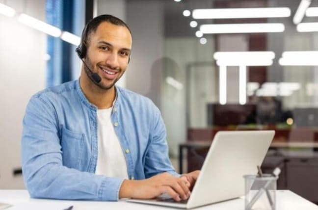 Smiling support agent with a headset working on a laptop